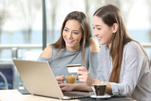 two teenage girls drinking coffee and shopping online using a laptop