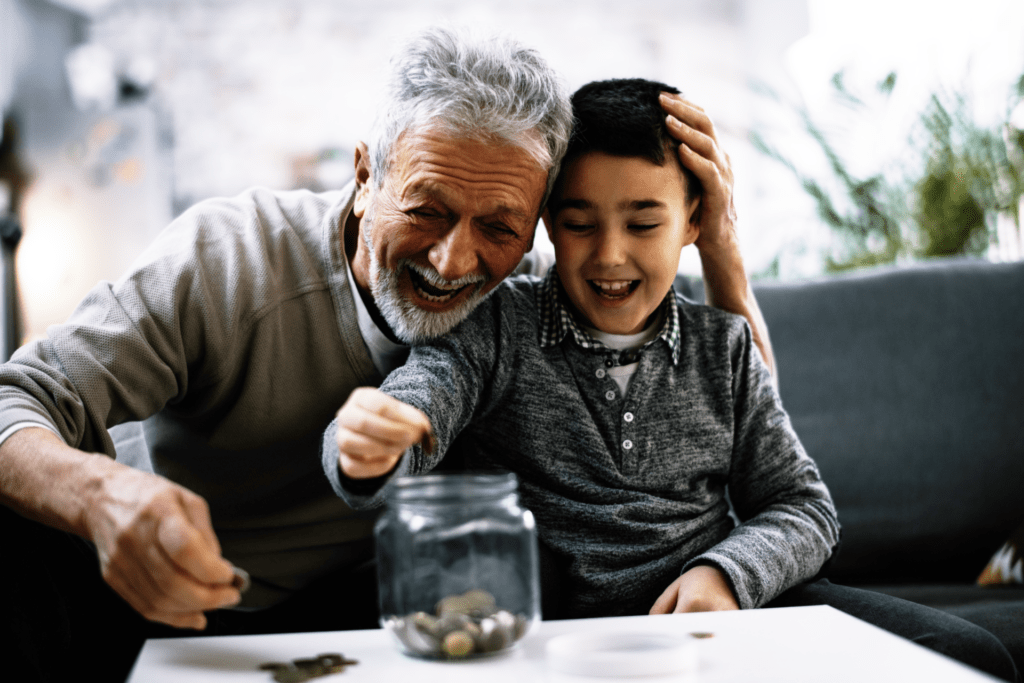 grandfather and grandson smiling, sitting on couch, counting lose change into a jar.