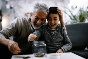 grandfather and grandson smiling, sitting on couch, counting lose change into a jar.
