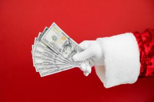Person-In-Santa-Clause-Suit-Holding-Out-Money-On-Red-Background