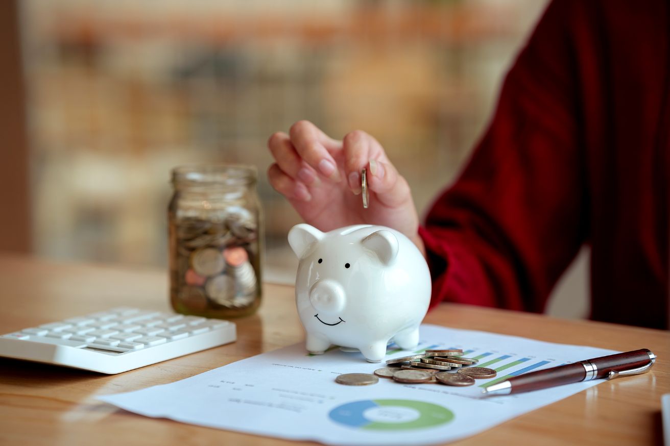 savings-account (1) close up image of a young woman planning her personal finances at home, using a piggy bank, calculator, and coins.